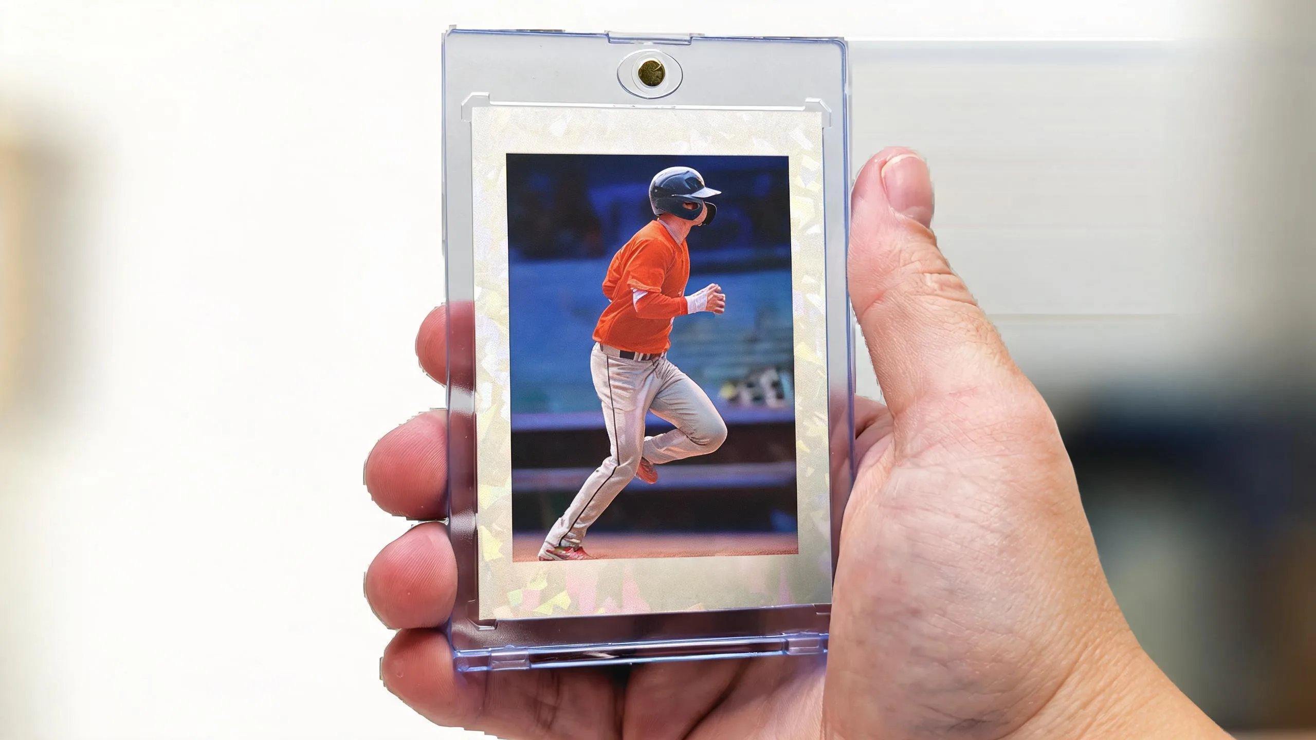 Hand holding a magnetic case with a chrome action-photo card, top 100 sports cards showcase.